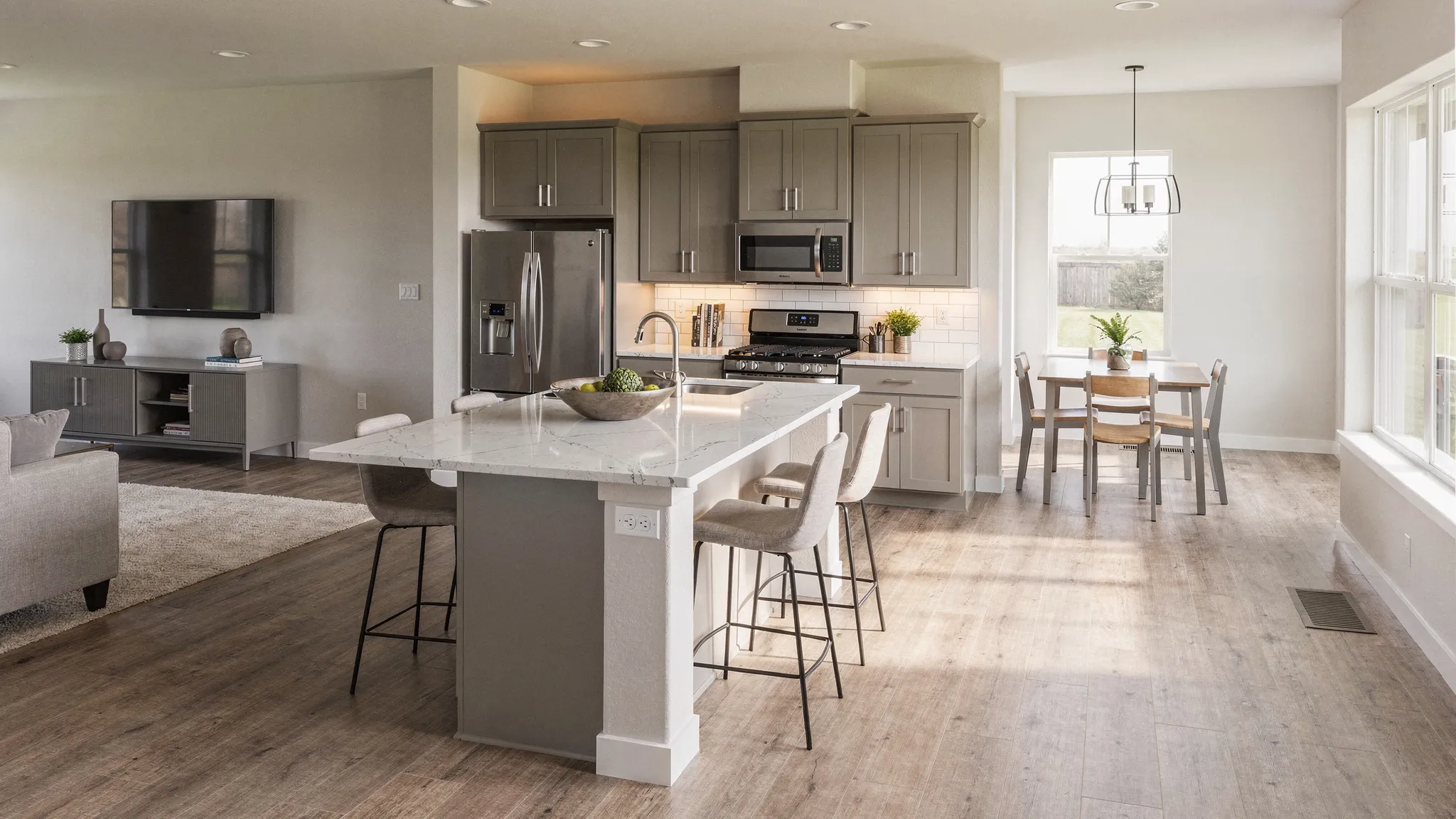 A bright, modern manufactured home interior with an open kitchen and living area, showing a large island, cabinet storage, and a clear walkway from entry to dining.