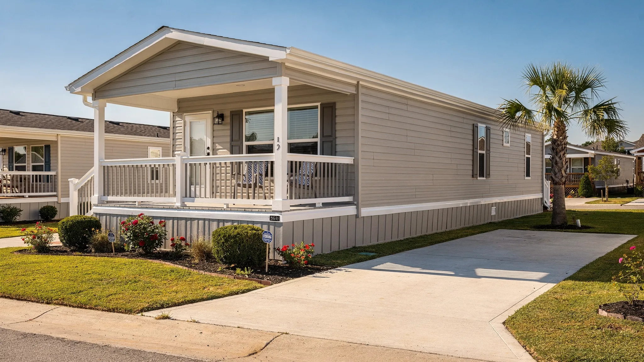 A well-maintained modern manufactured home exterior in a South Texas community setting with a small porch, clean skirting, and a neat driveway, photographed on a sunny day.