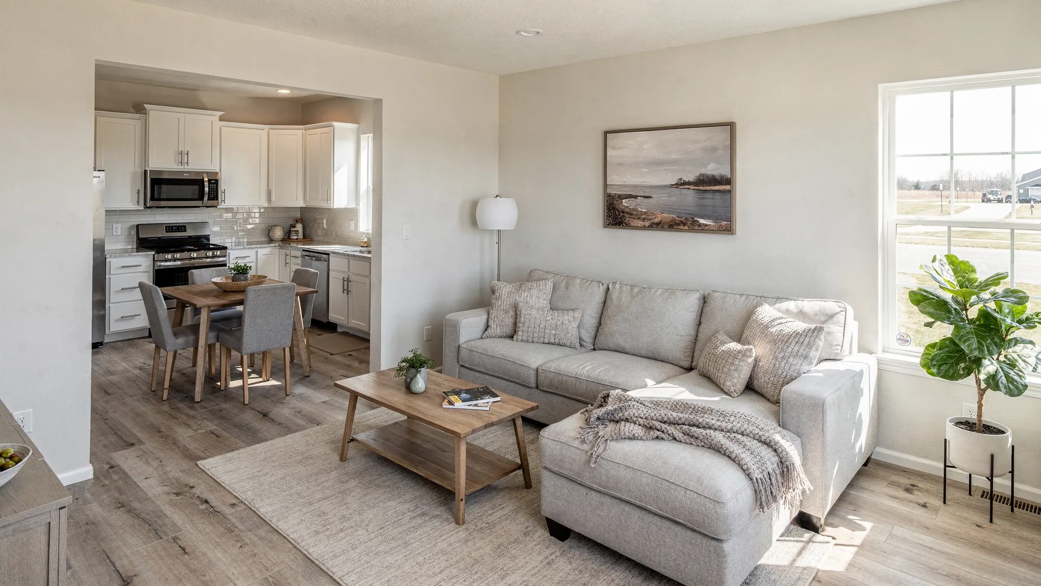 A bright, modern manufactured home living room with large windows, neutral walls, a cozy sofa, and an open view into a clean kitchen with a dining nook.