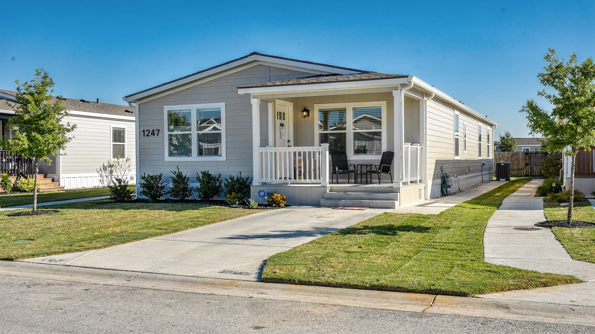 A clean manufactured home in a San Antonio-style community with a small front porch, driveway, trimmed lawn, and clear address numbers visible from the street.