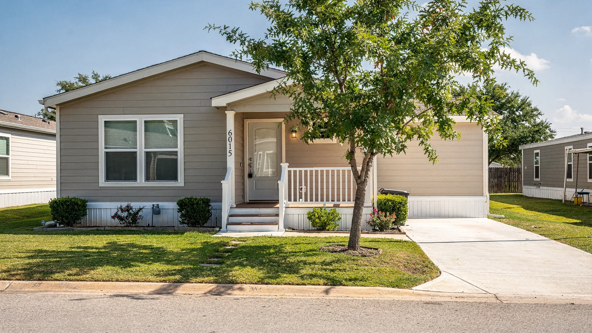 A manufactured home in a well-kept San Antonio community with a clean driveway, shaded yard, and visible exterior details that a renter would inspect before signing a lease.