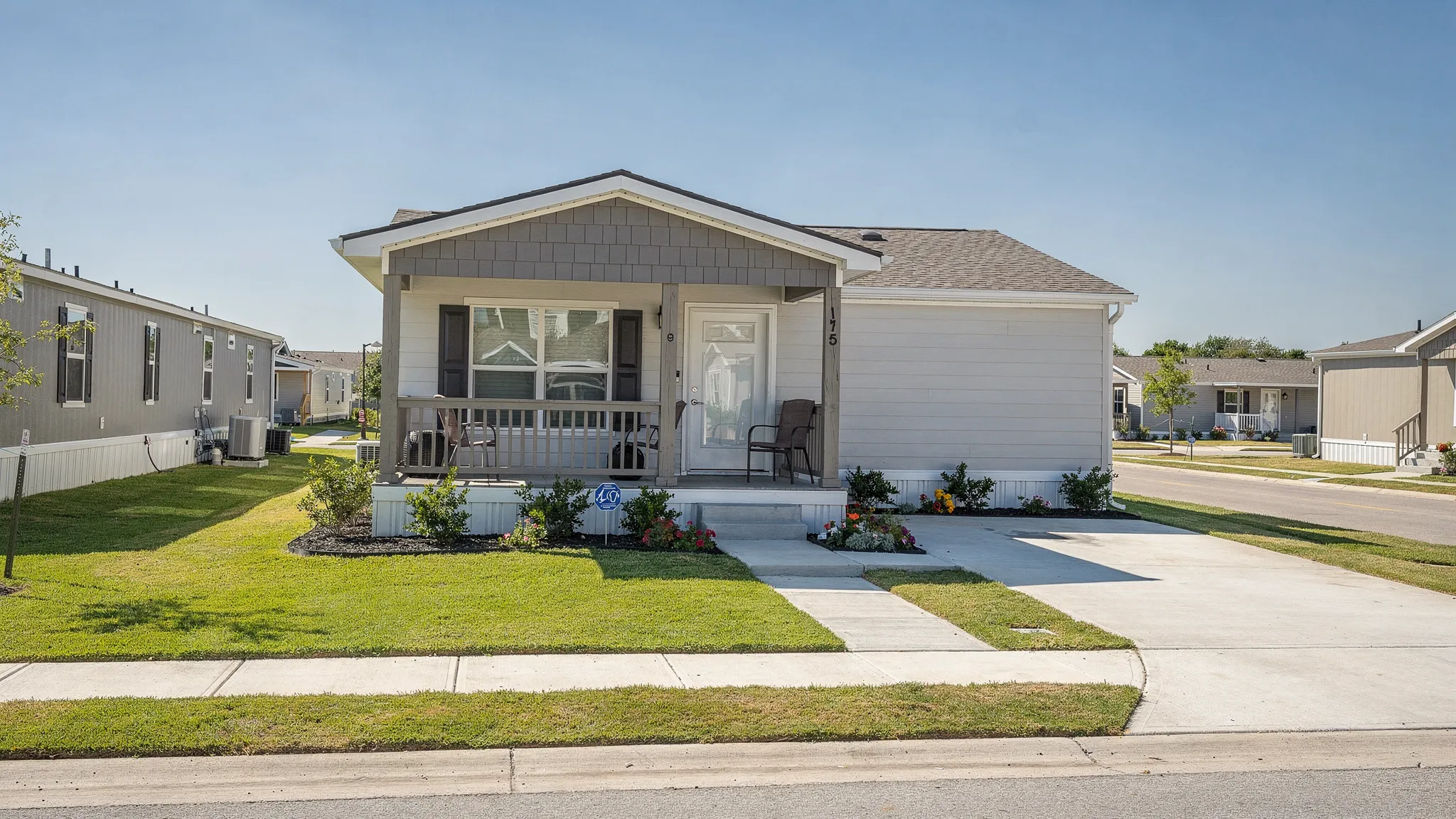 A modern manufactured home in a sunny San Antonio community with a small front porch, clean landscaping, and neighboring homes in the distance.