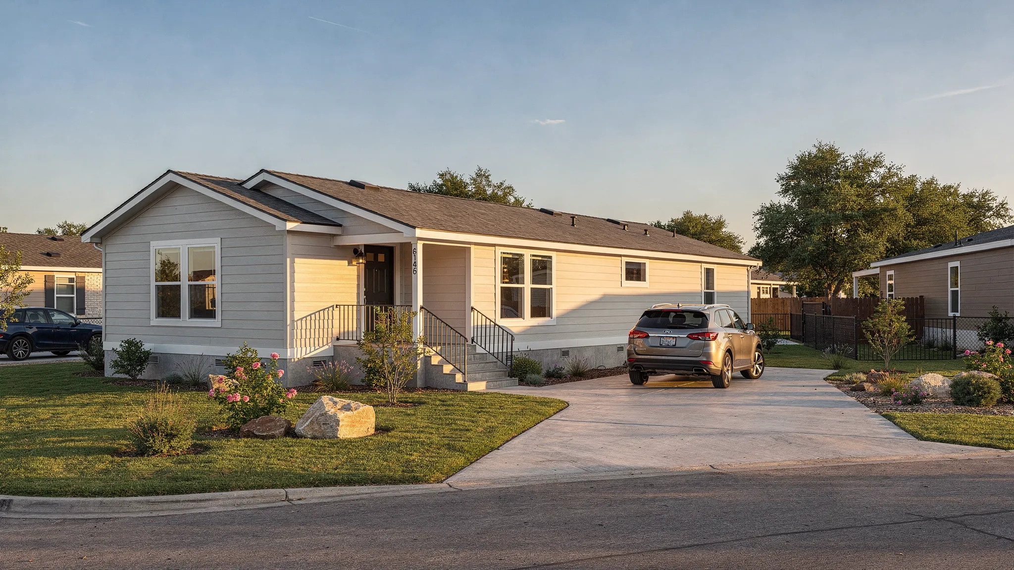 A modern manufactured home installed on a permanent foundation in a sunny San Antonio neighborhood, with a driveway, landscaped yard, and clear view of the home exterior.