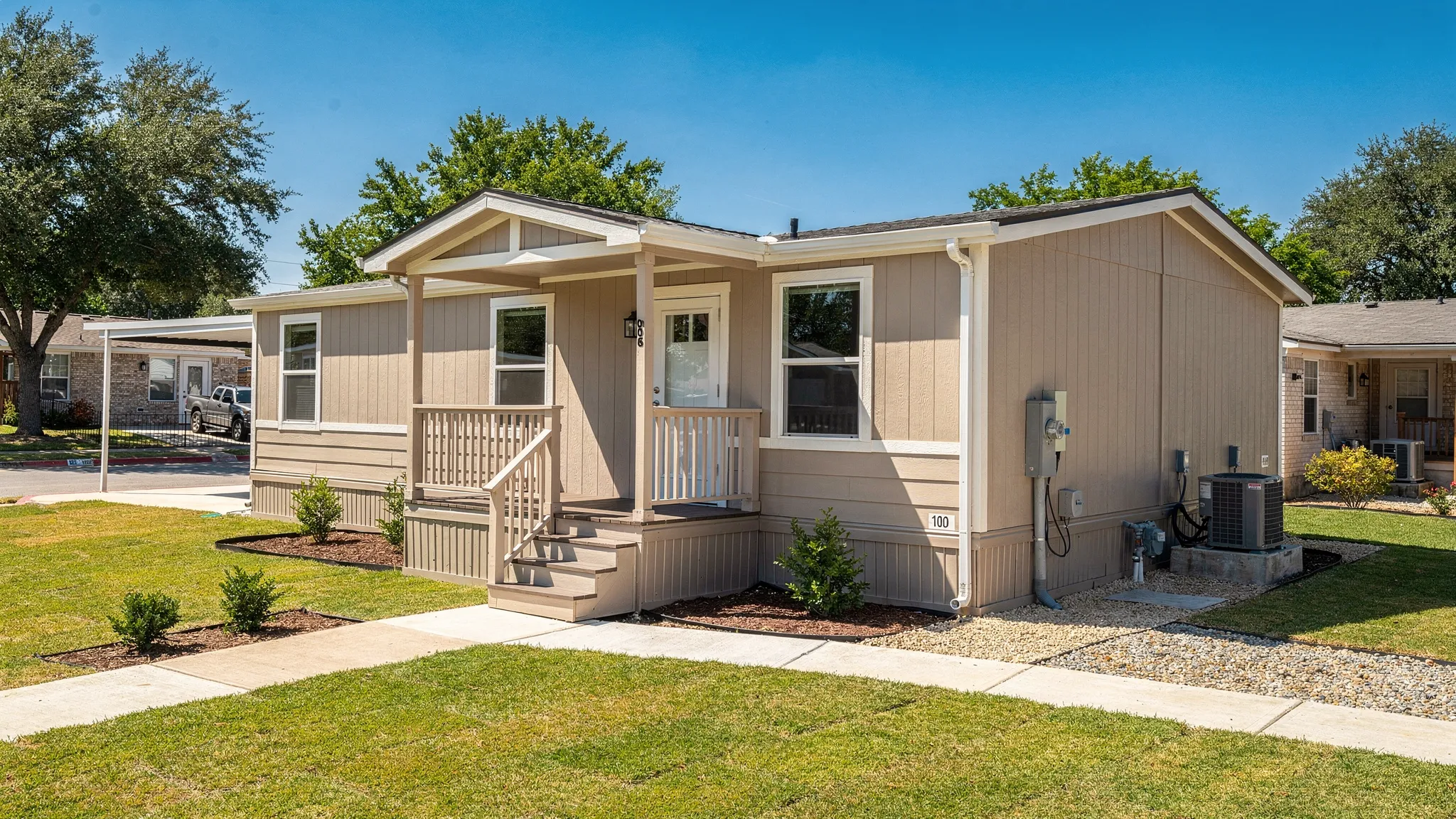 A single-wide manufactured home on a permanent foundation in a sunny San Antonio neighborhood, with a small porch, skirting, utility hookups, and clean landscaping.