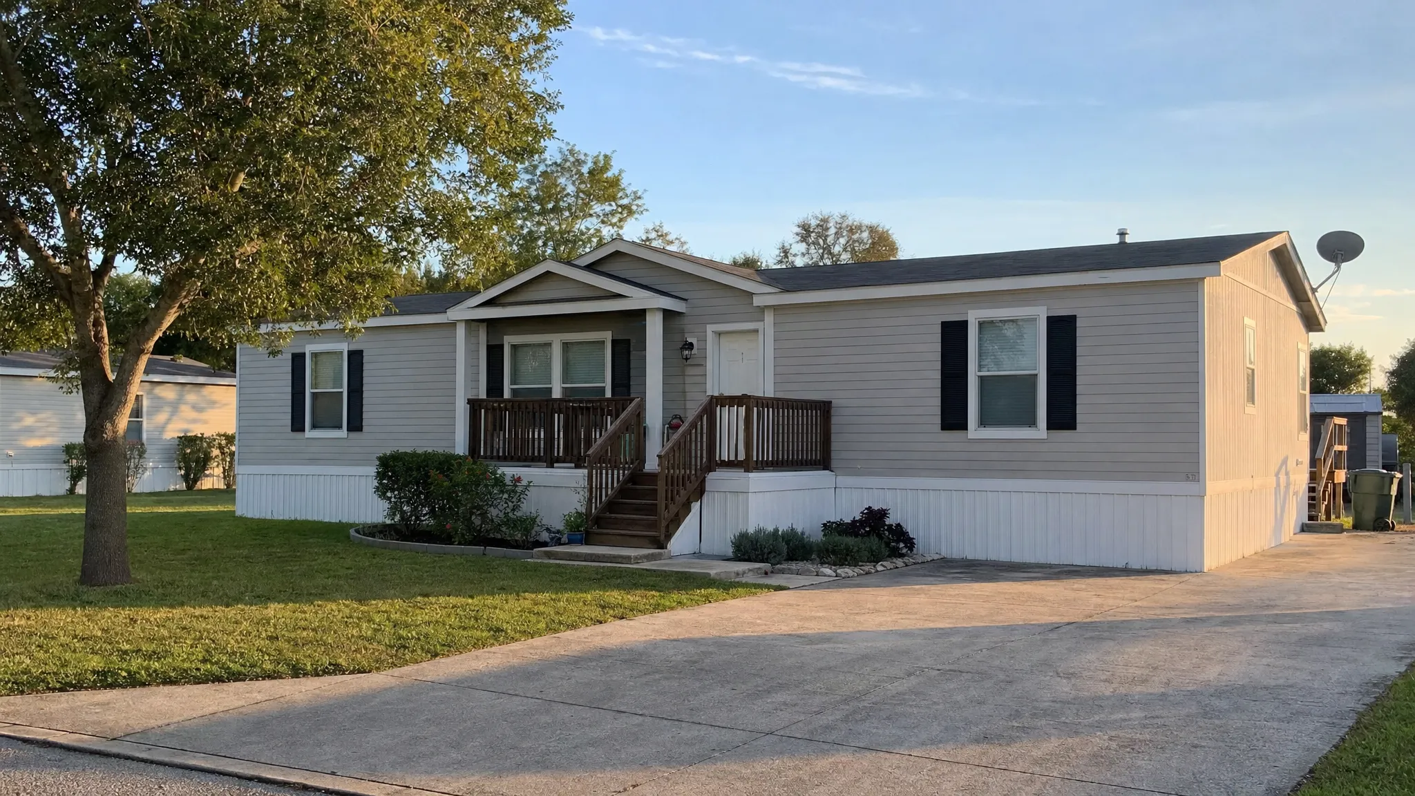 A double wide manufactured home in a quiet San Antonio-area community with a small front porch, driveway, trimmed lawn, and late afternoon light.