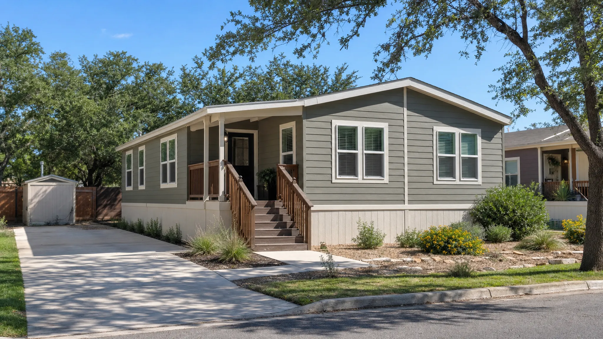 A double wide manufactured home on a residential lot with a small front porch, driveway, low landscaping, and a sunny San Antonio neighborhood setting.
