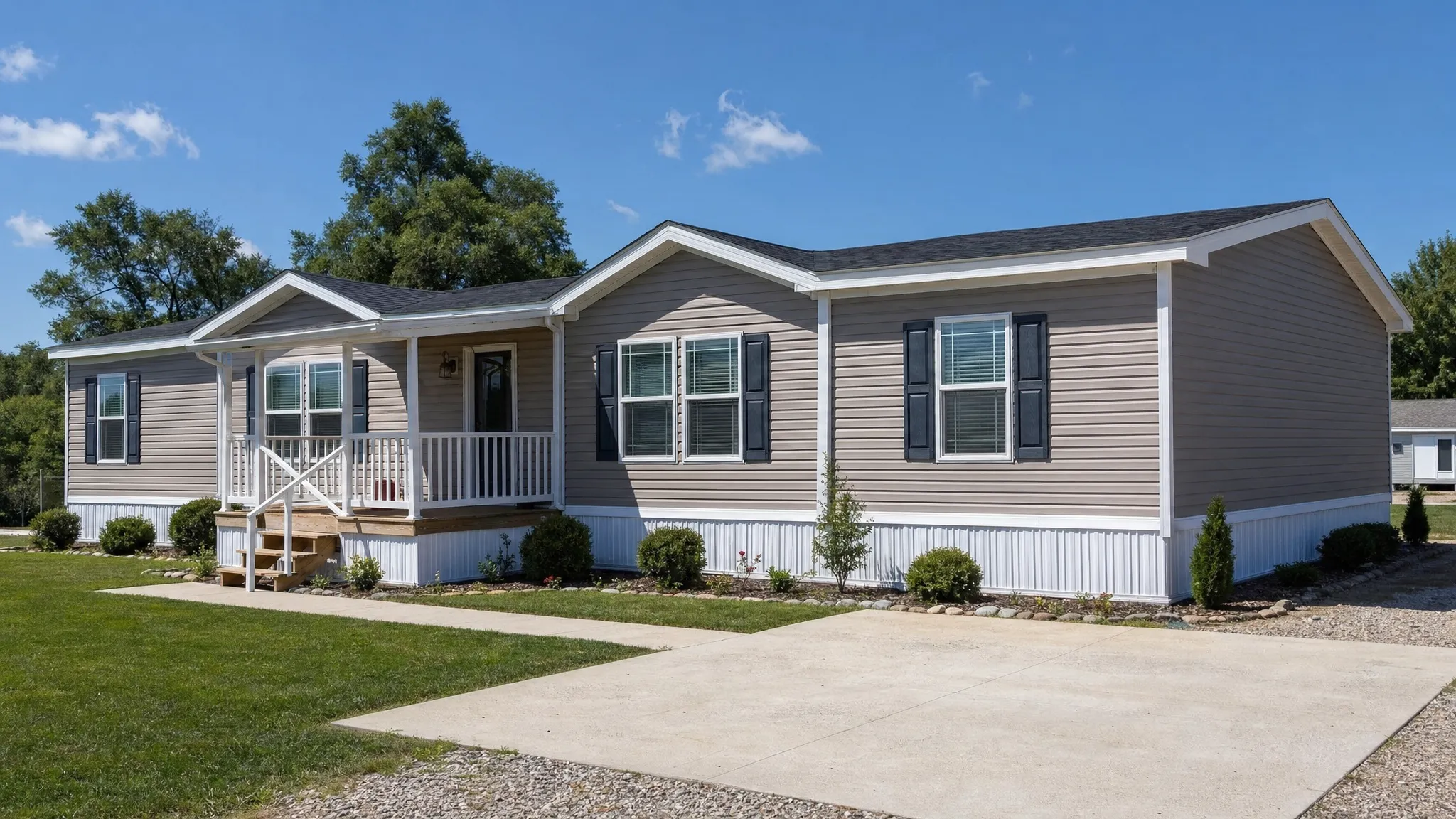 A double wide manufactured home viewed from the front corner on a prepared lot, with the joined sections visible, a front porch, a driveway, and trimmed grass around the home.