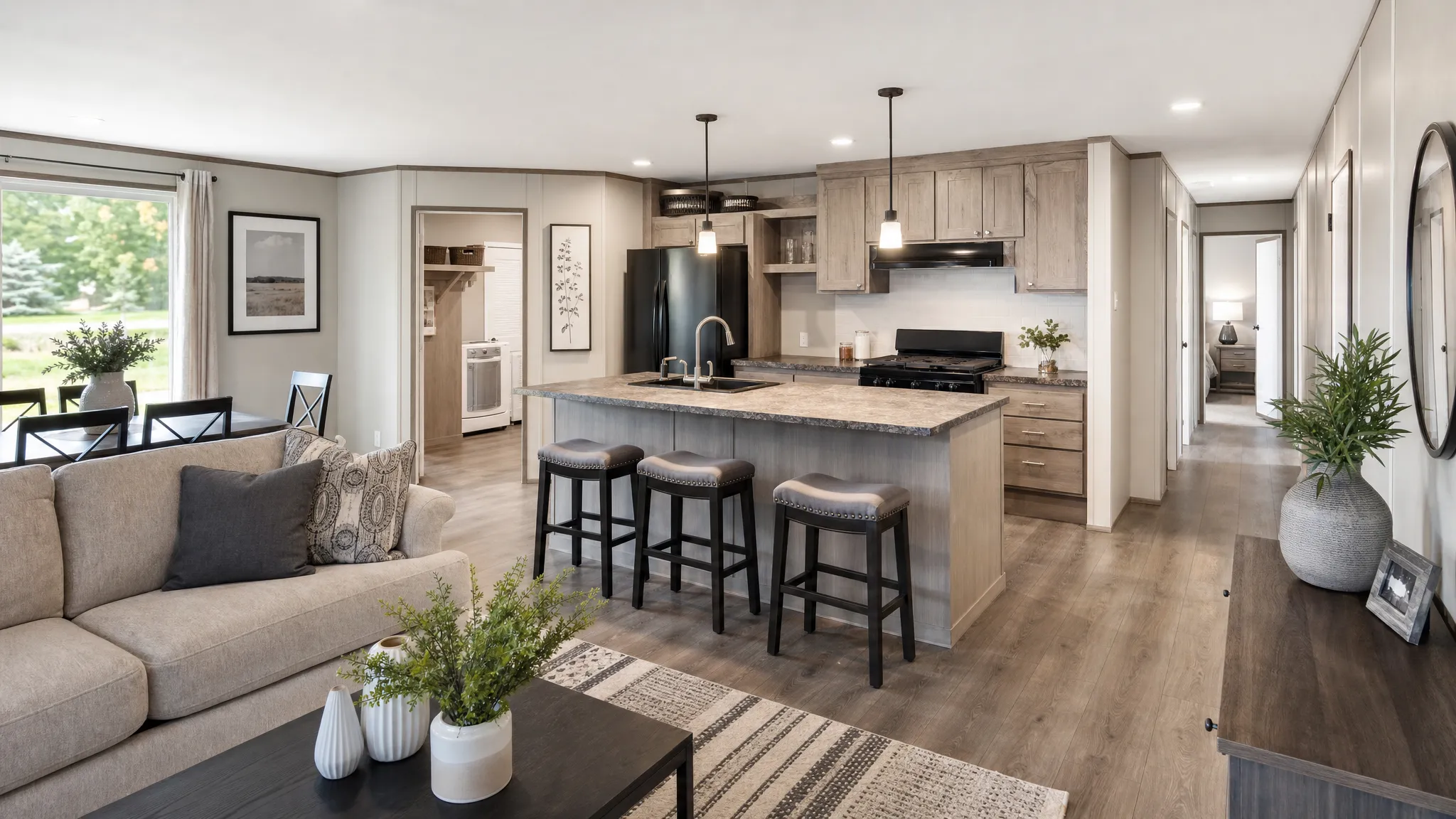 A modern double wide manufactured home interior with an open living area, kitchen island, wide hallway, and split-bedroom flow, shown from an eye-level view with natural light and a clear view into the connected rooms.