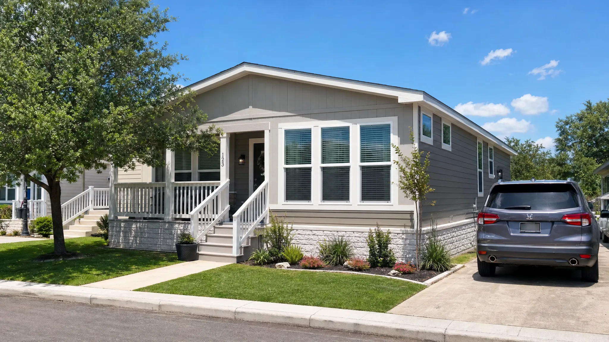 A modern manufactured home in a sunny San Antonio neighborhood with a small front porch, clean landscaping, wide windows, and a parked family vehicle in the driveway.