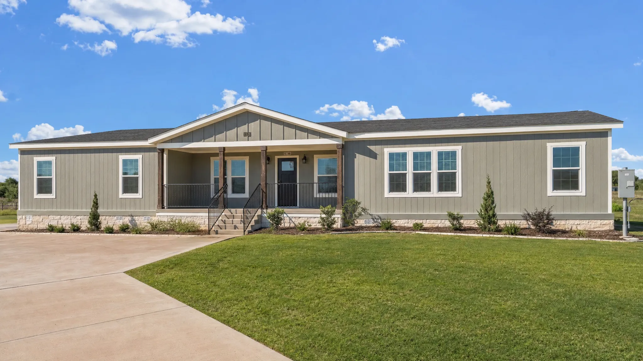 A modern manufactured home installed on a permanent foundation with a clean yard, driveway, utility connections, and open Texas sky in the background.