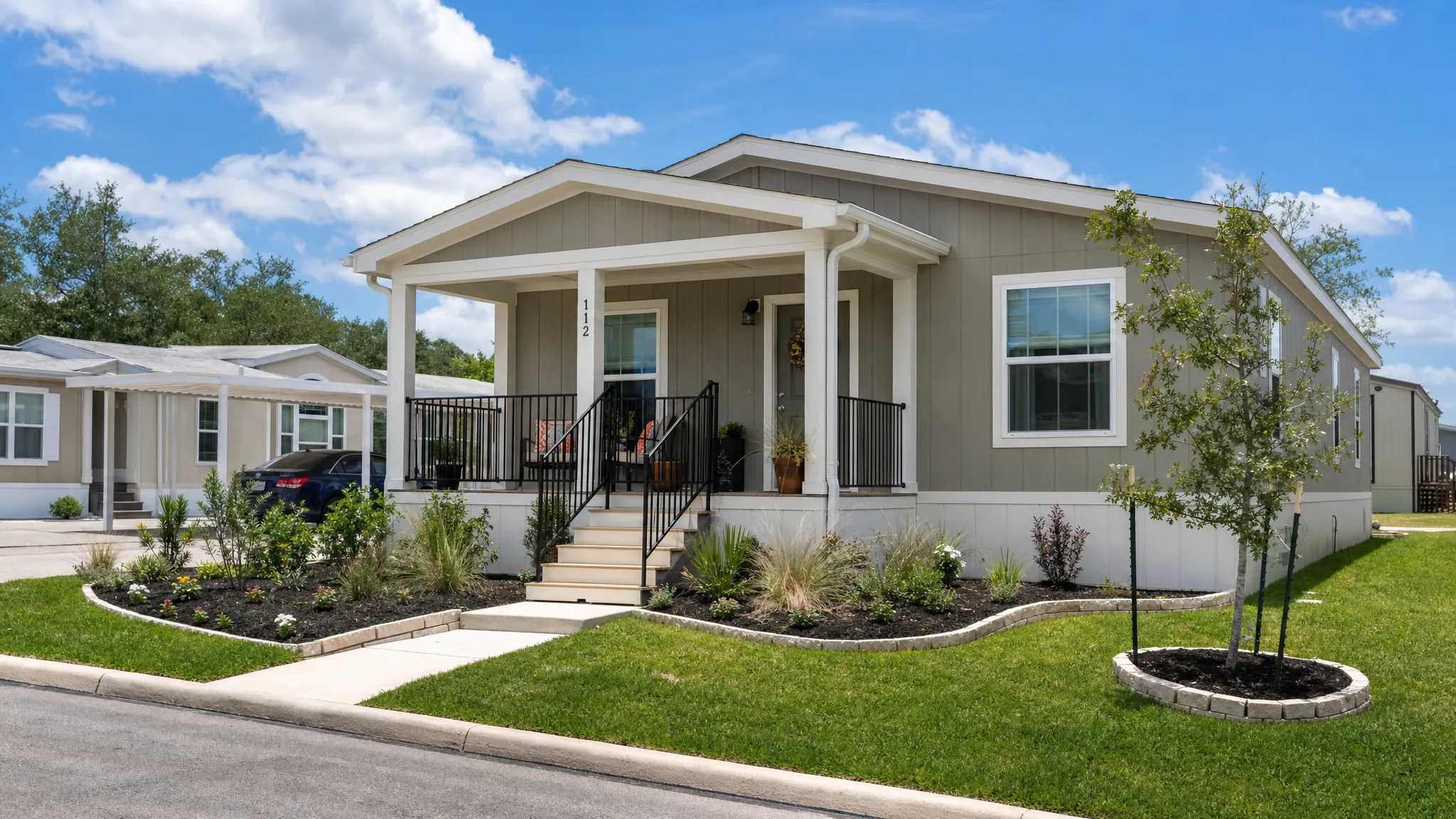 A modern manufactured home with a covered front porch, neat landscaping, and a family-friendly yard in a sunny San Antonio neighborhood.