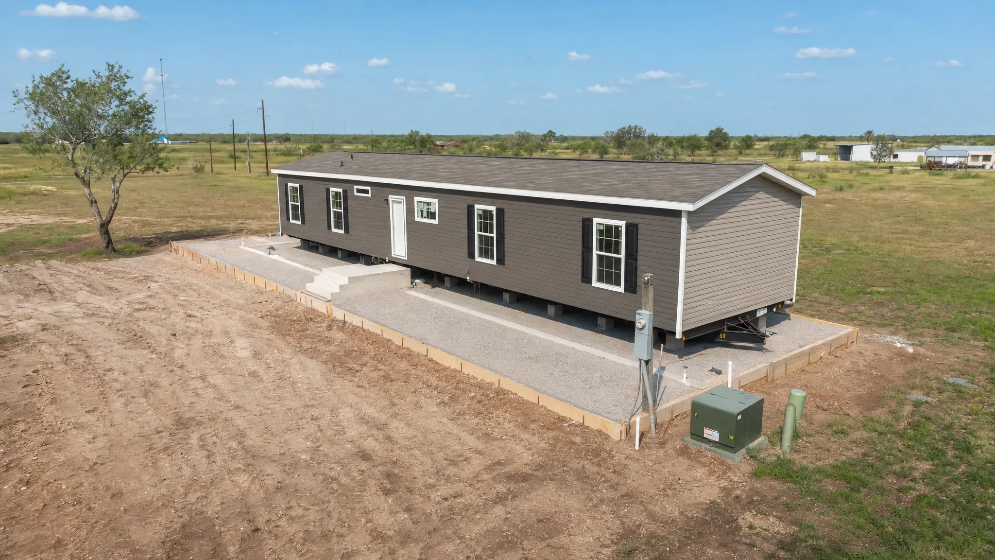 A new manufactured home being installed on a prepared homesite in South Texas, with the foundation area, utility connections, and open land around the home visible from a slightly elevated angle.