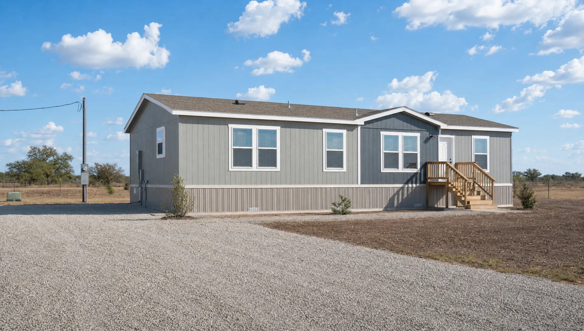 A modern manufactured home set on a prepared Texas lot with skirting, front steps, utility connections, a gravel driveway, and open land in the background.