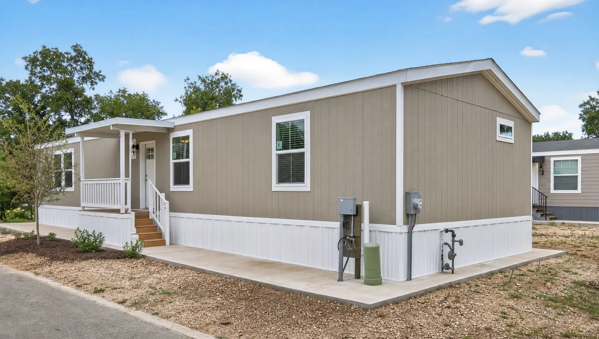 A single-wide manufactured home on a prepared homesite in a San Antonio community, with skirting, utility connections, a small front porch, and the foundation area clearly visible from the side.