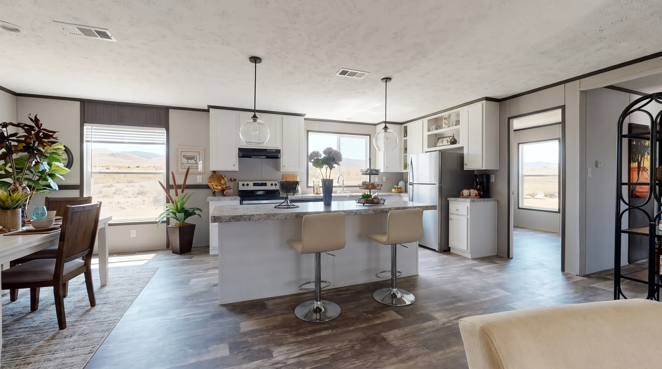 A bright manufactured home kitchen with a large center island, pendant lights, durable counters and an open view into the living area.