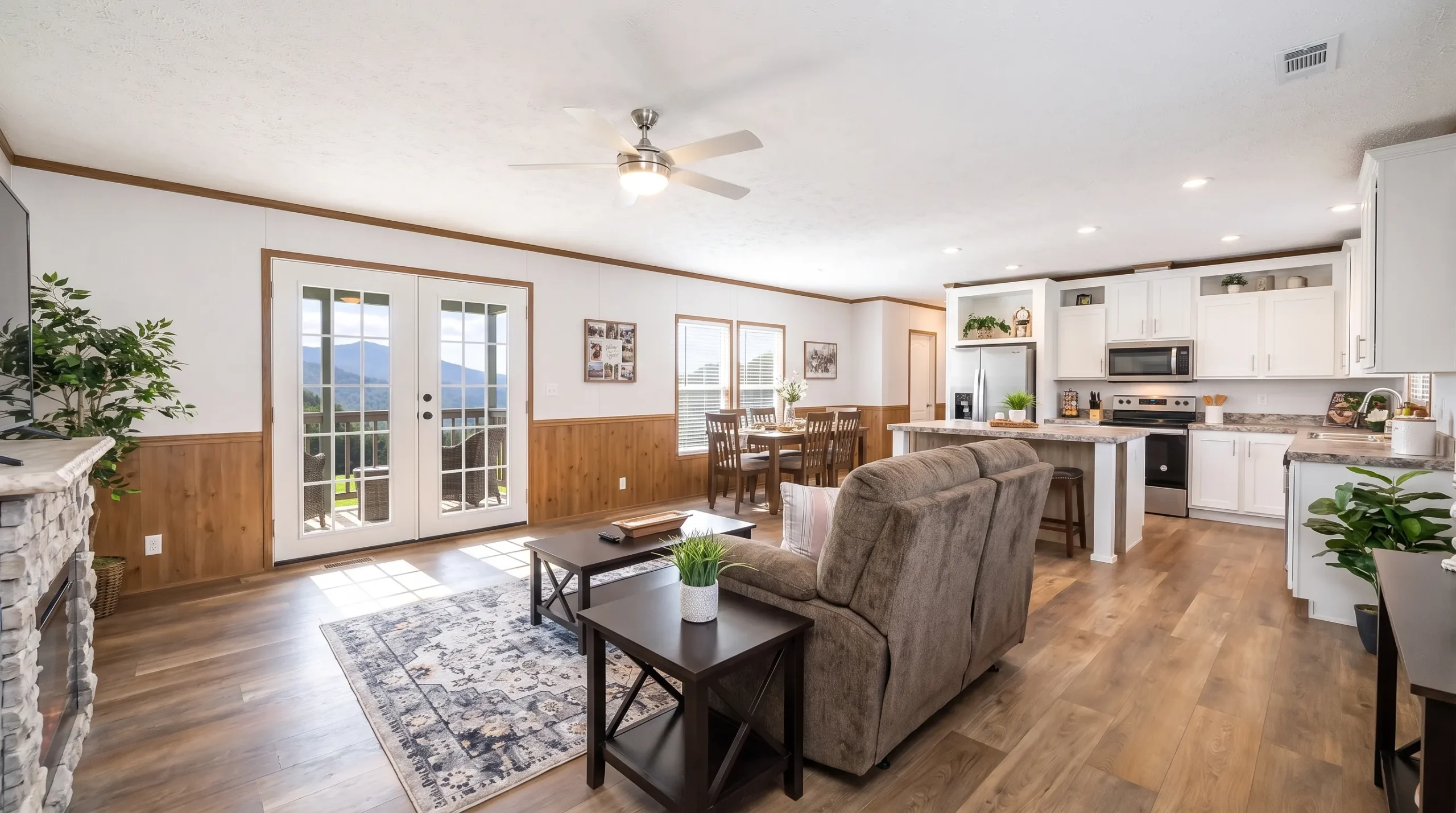 A bright open-plan double wide manufactured home interior with the kitchen, dining area, and living room connected in one continuous space, showing natural light, modern finishes, and room for everyday family use.