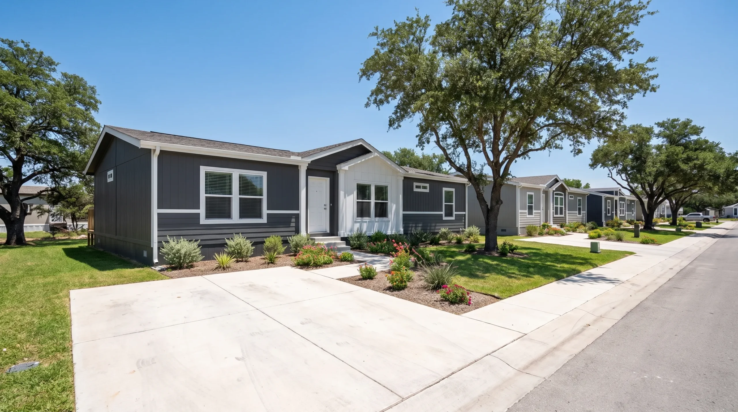 A clean manufactured home community shows modern doublewide homes, paved streets, small front yards, and mature trees in San Antonio.
