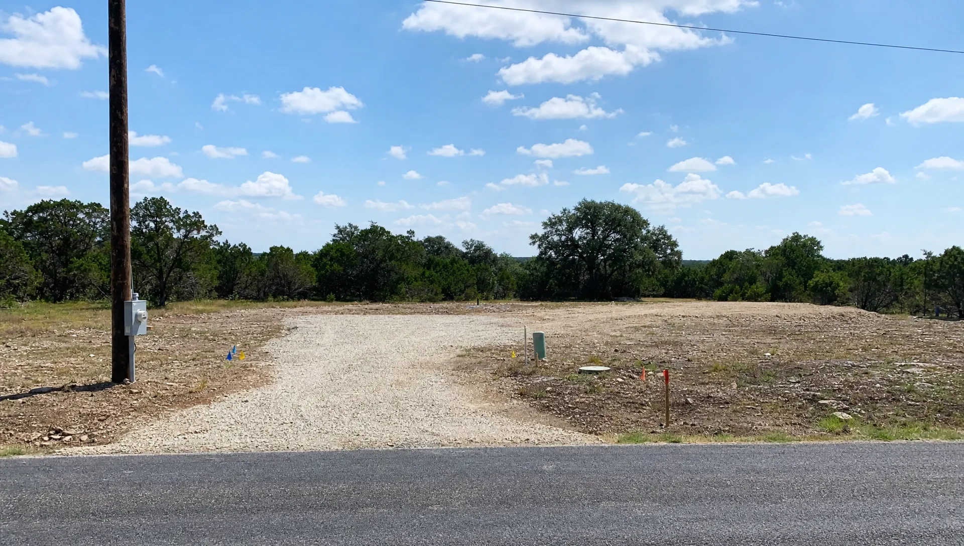 A cleared Texas homesite shows a gravel driveway, utility markings, a power pole, and an open pad area for a manufactured home.
