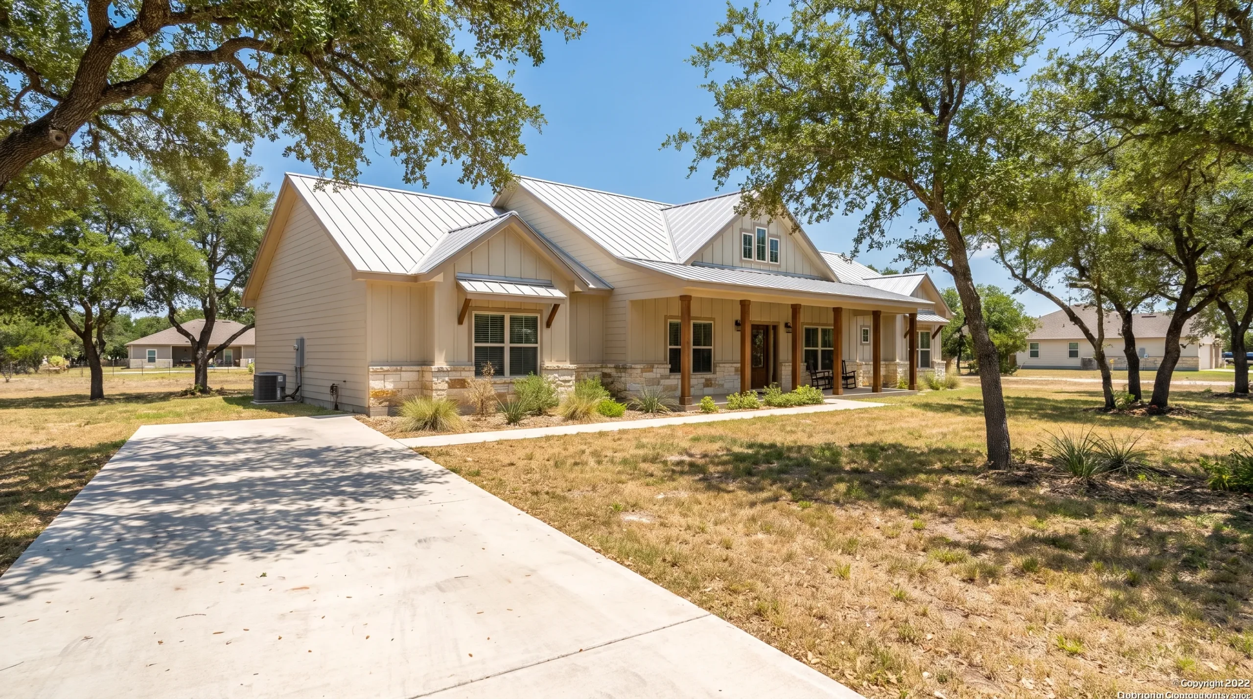 A modern doublewide manufactured home in a sunny San Antonio neighborhood with shade trees, light-colored exterior finishes, a covered entry, and open space around the home for airflow and maintenance.