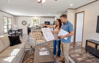 Two adults review a floor plan inside a model home while comparing room layout and budget fit.