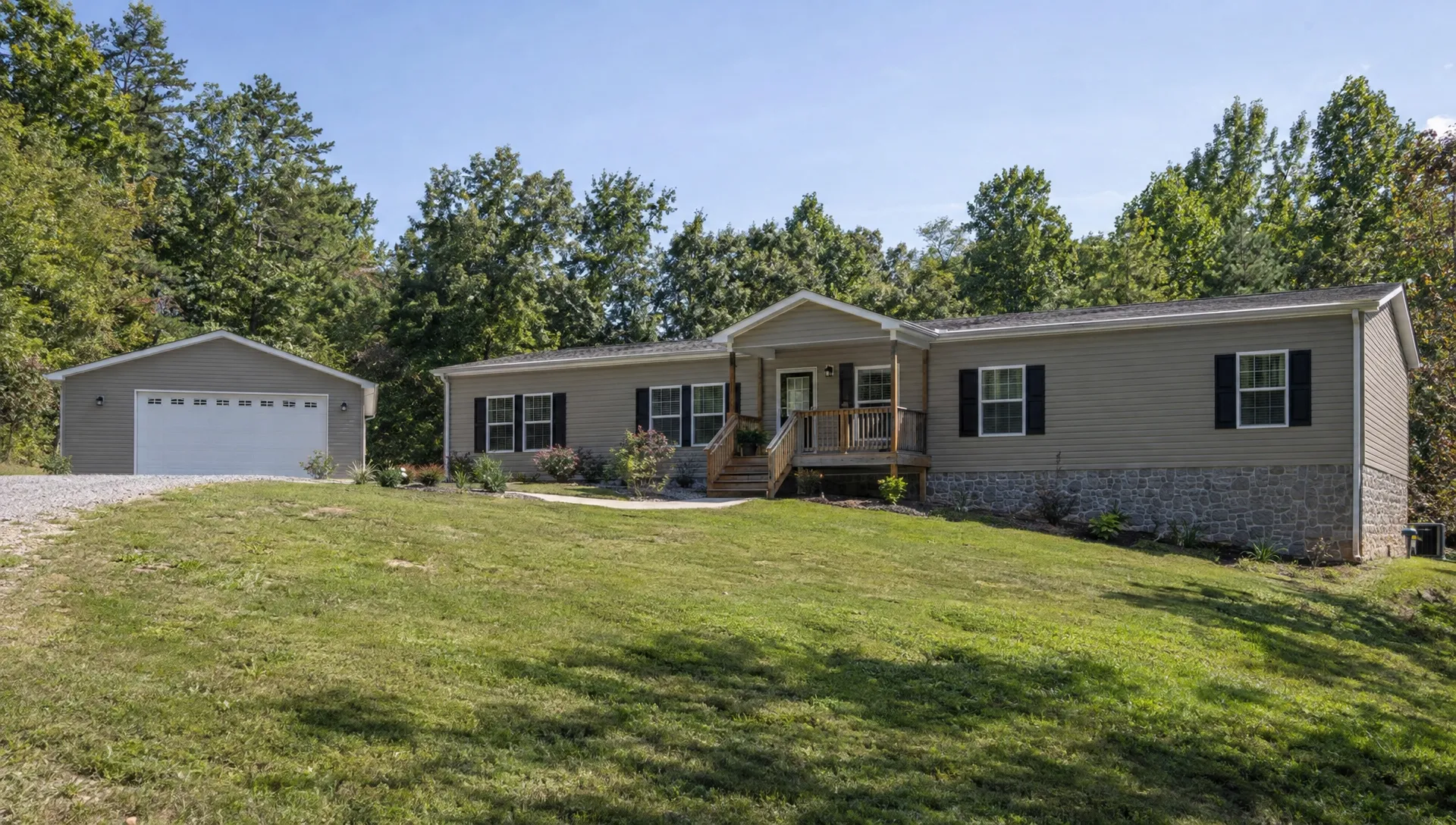 A three-section manufactured home has a covered entrance, a separate garage, and a graded yard that slopes away from its foundation.